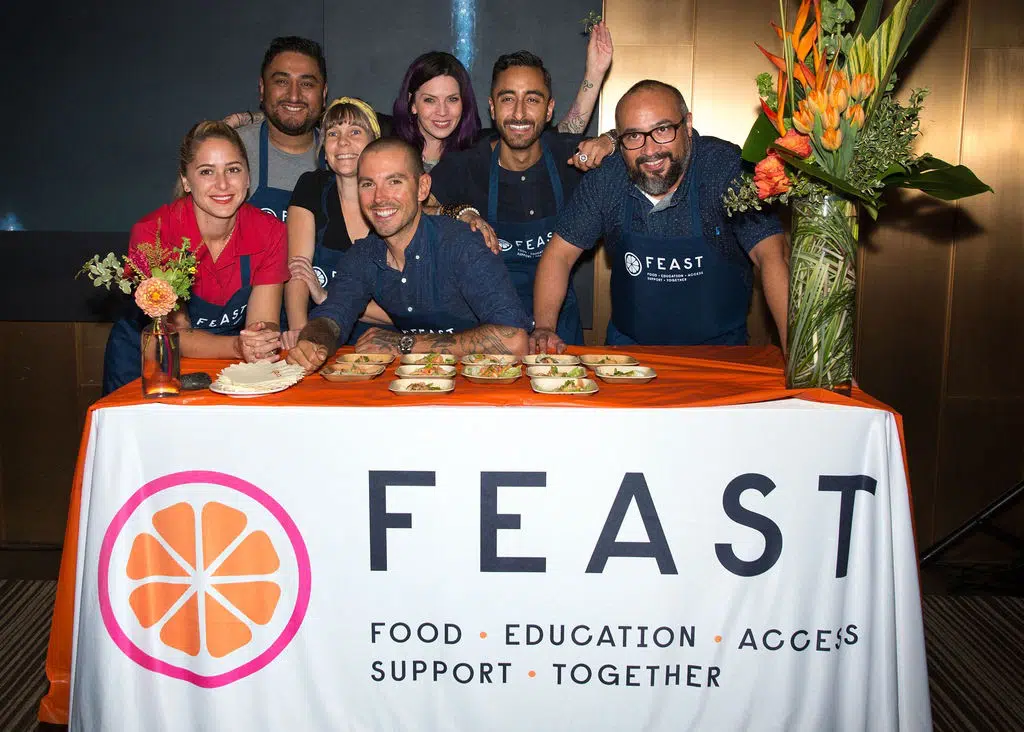 Sweetfin Chef Dakota Weiss (center) with FEAST’s collaborating chefs at FEAST’s 2019 Fall fundraiser leaning over a table with plated food.